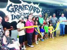 Cooper Blackledge, center with scissors, along with friends and family celebrated the opening of Graveyard Ink tattoo shop with a ribbon cutting on Friday. The group is standing in front of a graphic that was created by Korina Martin.
