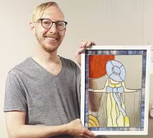 Adam Koci of Emporia holds “Prairie Stroll,” one of seven stained glass pieces now on display in the Council Grove Republican windows through Street Gallery KS, a division of the Bowers Center.