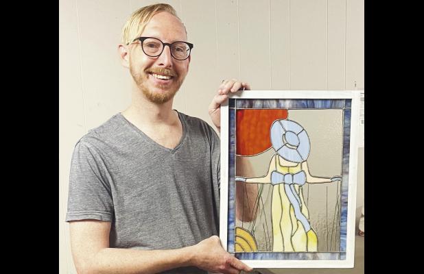 Adam Koci of Emporia holds “Prairie Stroll,” one of seven stained glass pieces now on display in the Council Grove Republican windows through Street Gallery KS, a division of the Bowers Center.